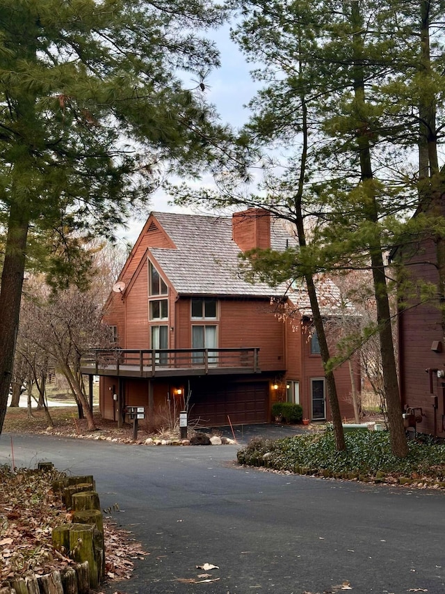 view of front of home with a deck, a garage, a chimney, and driveway