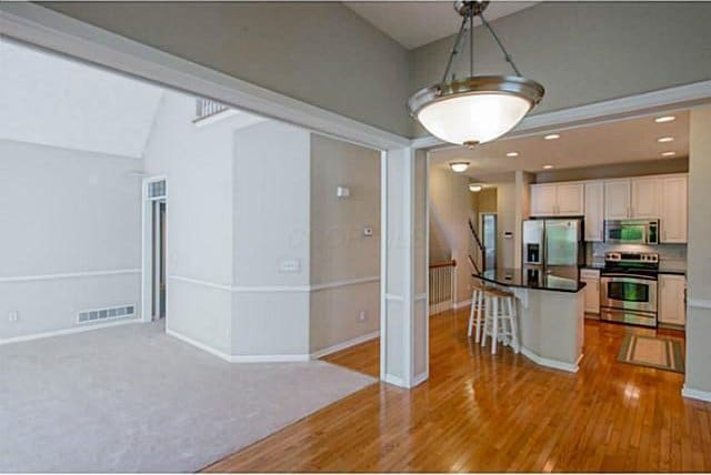 1139 Cross Creeks Rdg, Pickerington, OH 43147 - kitchen with appliances with stainless steel finishes, a breakfast bar, dark countertops, wood finished floors, and open floor plan