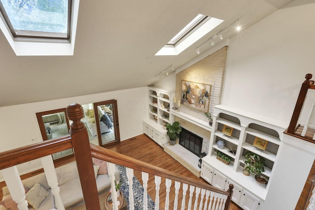 living room with a skylight, track lighting, wood finished floors, vaulted ceiling, and a fireplace with raised hearth