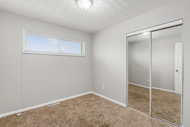 unfurnished bedroom featuring carpet flooring, a closet, a textured ceiling, visible vents, and baseboards