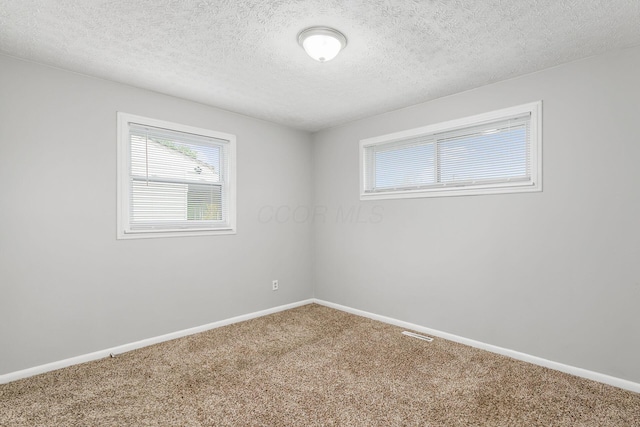 carpeted spare room featuring a textured ceiling, baseboards, and visible vents