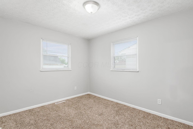 carpeted spare room featuring a textured ceiling, visible vents, and baseboards