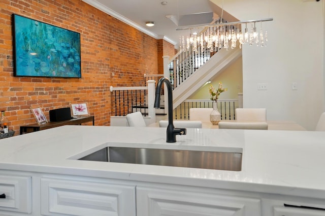 931 Dennison Ave, Columbus, OH 43201 - kitchen featuring a notable chandelier, brick wall, a sink, white cabinetry, and crown molding