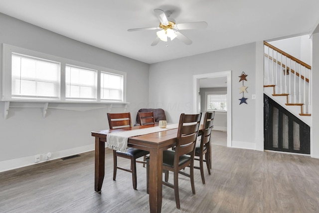 dining area featuring wood finished floors, visible vents, stairway, a ceiling fan, and baseboards