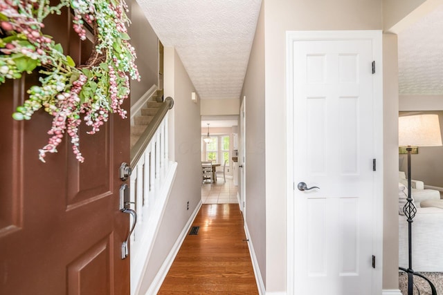 hallway featuring a textured ceiling, stairway, wood finished floors, and baseboards