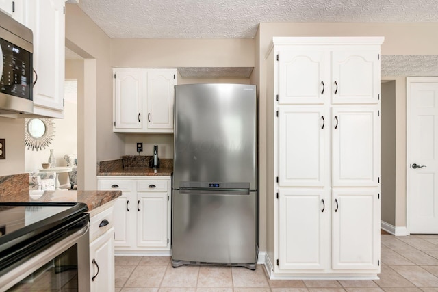 kitchen featuring appliances with stainless steel finishes, dark stone countertops, light tile patterned flooring, white cabinetry, and a textured ceiling