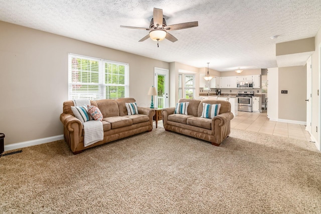 living area with a ceiling fan, light carpet, a textured ceiling, and baseboards