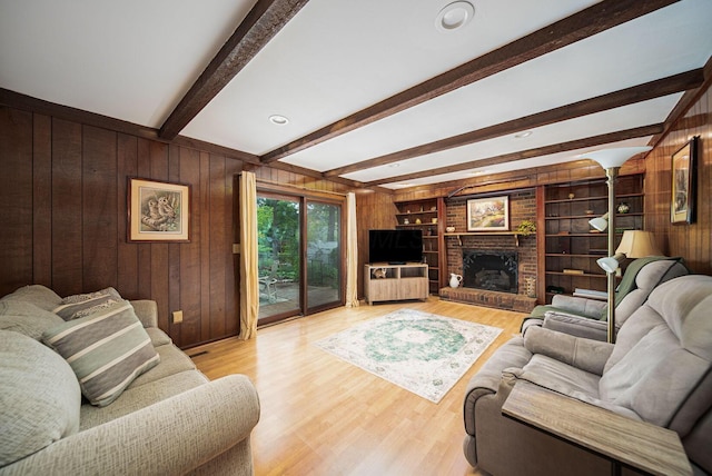living area featuring wood walls, beam ceiling, light wood-type flooring, and a fireplace