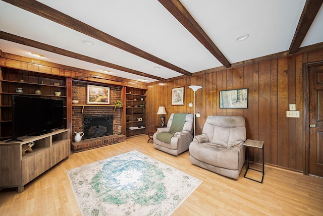 living room featuring beamed ceiling, a fireplace, wooden walls, and light wood finished floors