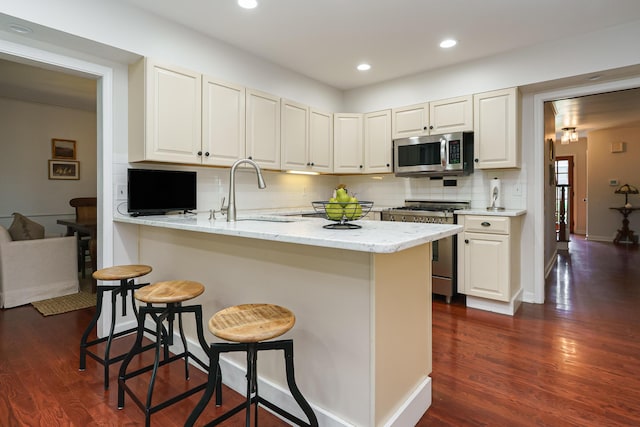 1660 Ridgeway Pl, Columbus, OH 43212 - kitchen with stainless steel appliances, decorative backsplash, a breakfast bar, dark wood-type flooring, and a peninsula