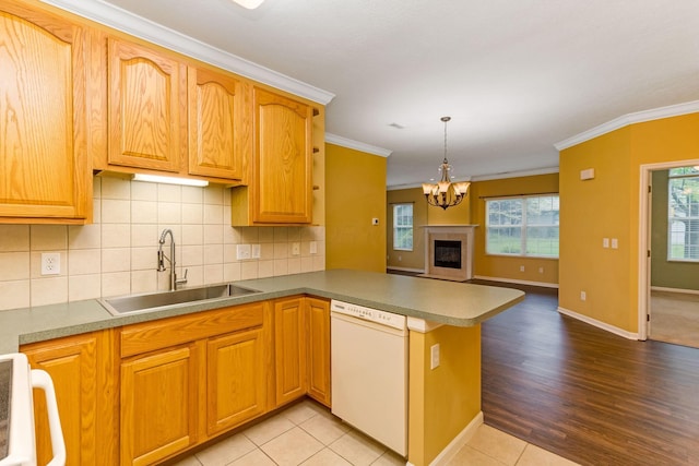 kitchen with white dishwasher, a sink, a peninsula, crown molding, and backsplash
