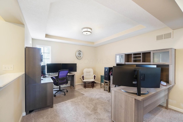 carpeted home office featuring a tray ceiling and baseboards