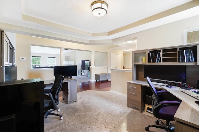 carpeted home office featuring ornate columns, a raised ceiling, and baseboards