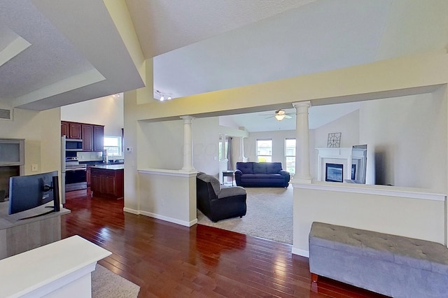 living area with decorative columns, dark wood-style flooring, baseboards, a glass covered fireplace, and a ceiling fan