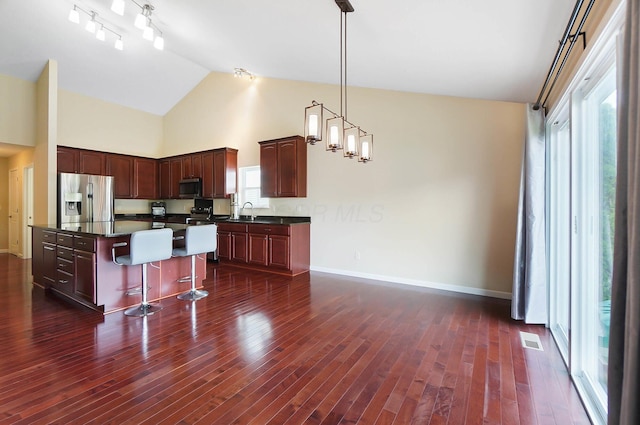 kitchen with appliances with stainless steel finishes, dark countertops, baseboards, a sink, and high vaulted ceiling