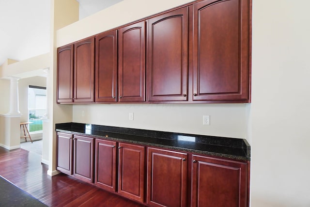 kitchen with dark brown cabinets, dark wood-type flooring, dark stone counters, and baseboards