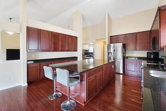 kitchen featuring stainless steel refrigerator with ice dispenser, high vaulted ceiling, a kitchen island, dark brown cabinets, and dark wood-type flooring
