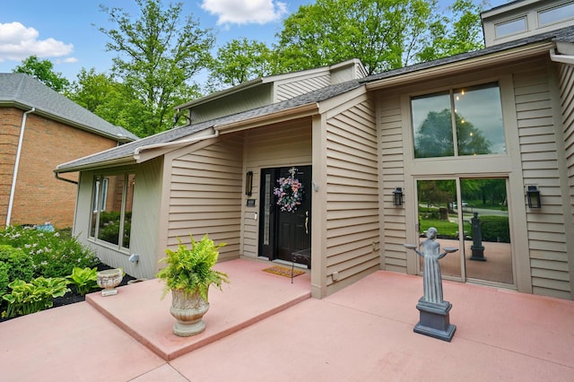 entrance to property with a patio and a shingled roof