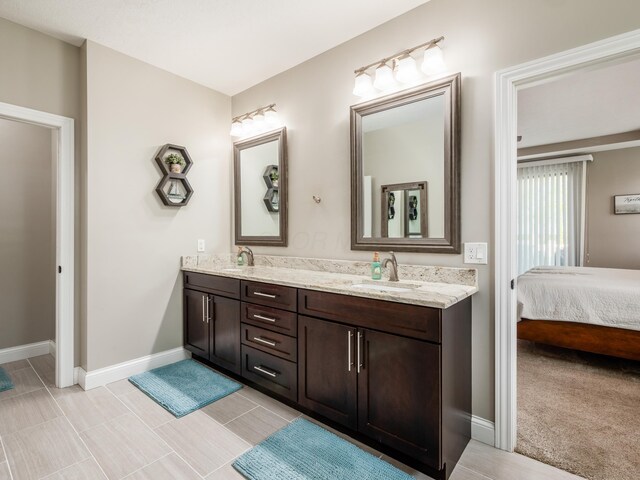 ensuite bathroom featuring baseboards and double vanity