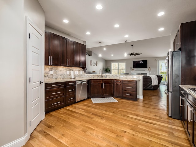 kitchen featuring appliances with stainless steel finishes, open floor plan, a peninsula, a sink, and light wood-style floors