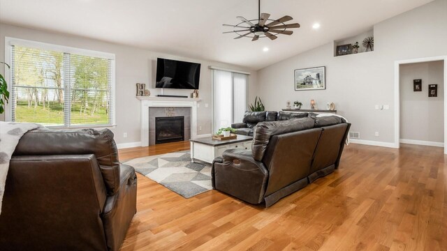 living area featuring vaulted ceiling, a fireplace, light wood-style flooring, ceiling fan, and baseboards