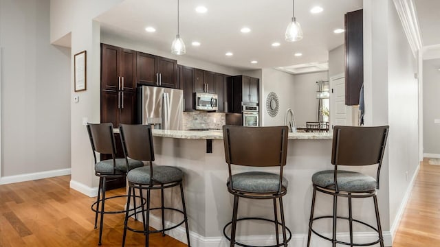 kitchen with appliances with stainless steel finishes, dark brown cabinets, recessed lighting, light wood-style flooring, and backsplash