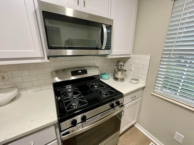 kitchen with stainless steel appliances, light stone counters, light wood finished floors, white cabinetry, and decorative backsplash