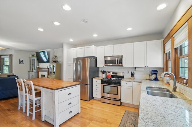 kitchen featuring appliances with stainless steel finishes, a sink, butcher block countertops, white cabinetry, and a breakfast bar