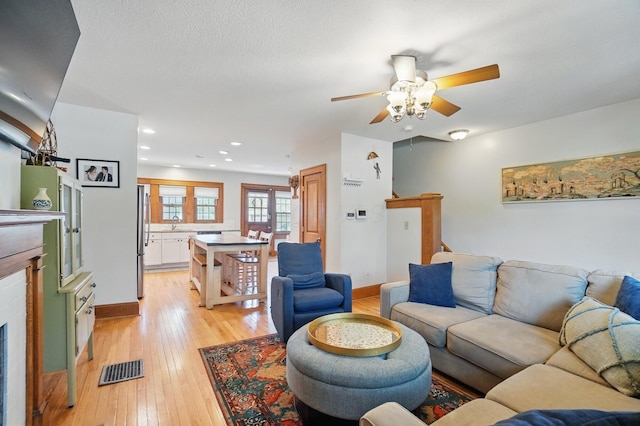 living area featuring a ceiling fan, light wood-style floors, baseboards, a fireplace, and recessed lighting