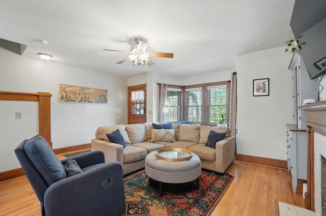 living area featuring baseboards, light wood-style flooring, a fireplace with flush hearth, and a ceiling fan