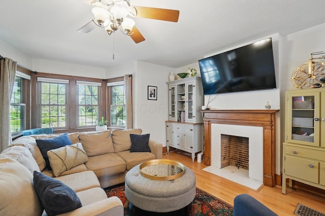 living room with ceiling fan, a fireplace with flush hearth, and light wood-style floors