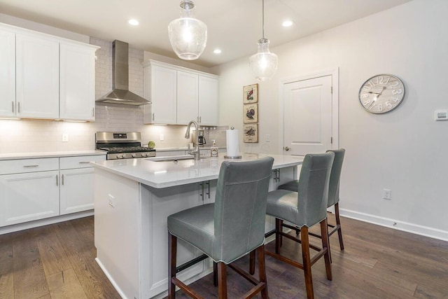 kitchen featuring a sink, gas range, dark wood-type flooring, backsplash, and wall chimney range hood