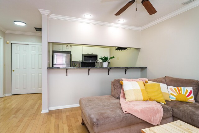 living area with light wood finished floors, crown molding, baseboards, and a ceiling fan