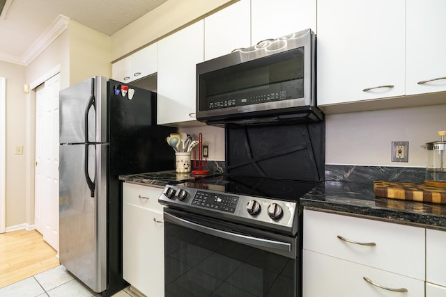kitchen featuring stainless steel appliances, dark stone countertops, crown molding, white cabinetry, and light tile patterned floors