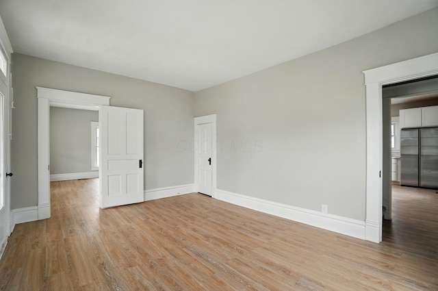 unfurnished bedroom featuring light wood-style flooring, baseboards, and stainless steel refrigerator