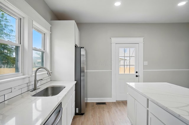 kitchen with light stone countertops, light wood finished floors, visible vents, a sink, and stainless steel appliances