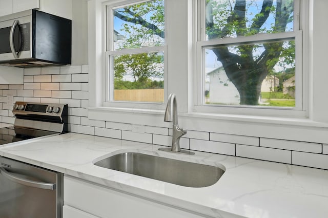 kitchen featuring a sink, a healthy amount of sunlight, backsplash, white cabinets, and appliances with stainless steel finishes