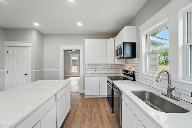 kitchen featuring a sink, stainless steel appliances, tasteful backsplash, light wood-style flooring, and white cabinetry