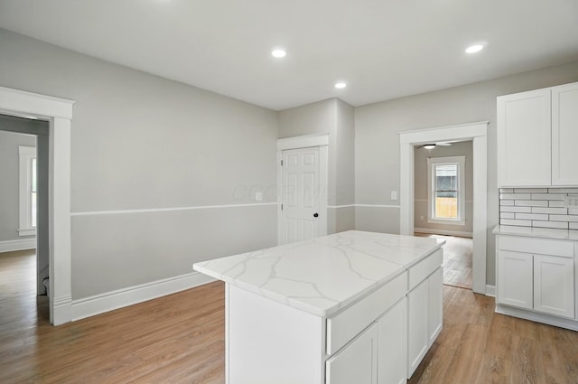 kitchen featuring recessed lighting, light wood finished floors, white cabinetry, light stone countertops, and a kitchen island