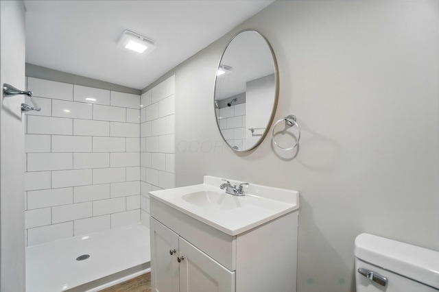 bathroom featuring toilet, a tile shower, and vanity