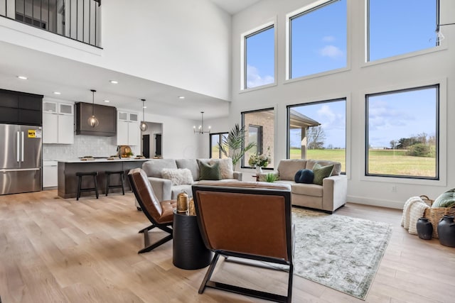 living room with an inviting chandelier, light wood-type flooring, and a towering ceiling