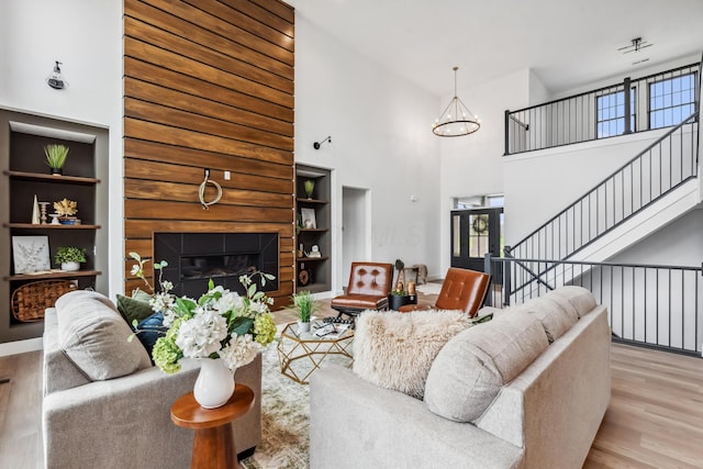 living room featuring a towering ceiling, a notable chandelier, a glass covered fireplace, and wood finished floors