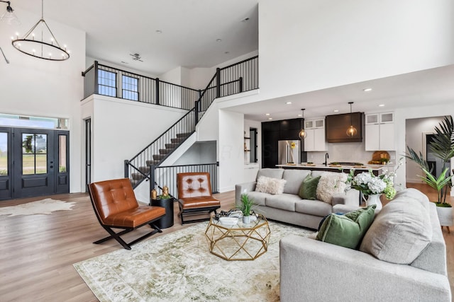 living area with a notable chandelier, light wood-style flooring, recessed lighting, stairway, and a high ceiling
