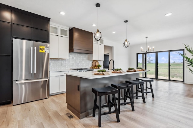 kitchen featuring stainless steel refrigerator, a breakfast bar area, backsplash, light countertops, and light wood-type flooring