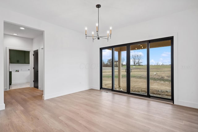 spare room featuring light wood-style floors, a chandelier, and plenty of natural light