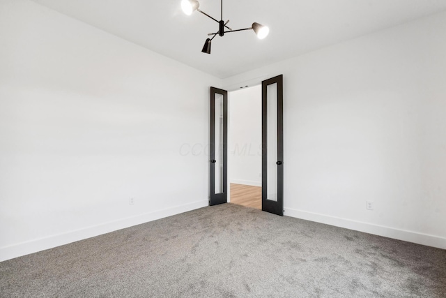 carpeted empty room featuring a chandelier and baseboards
