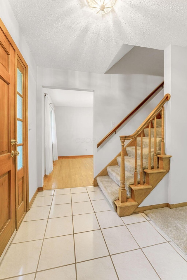entrance foyer featuring stairs, baseboards, a textured ceiling, and light tile patterned flooring
