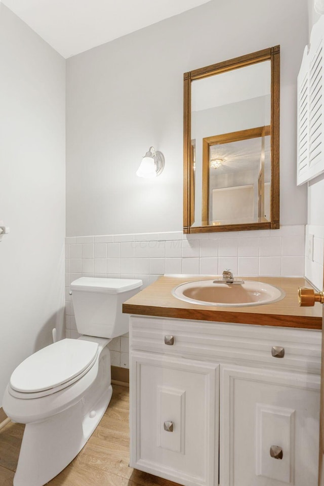 bathroom featuring tile walls, toilet, vanity, a wainscoted wall, and wood finished floors
