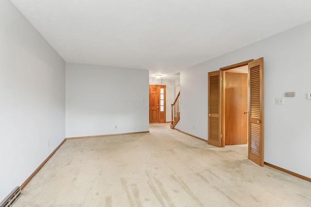 spare room with light colored carpet, stairway, and baseboards