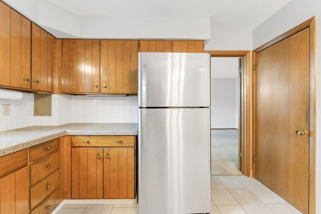 kitchen with freestanding refrigerator, light countertops, tasteful backsplash, and brown cabinetry